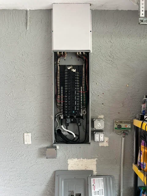 Electrical panel installation with breaker box, organized wiring, and white cover plate on concrete wall
