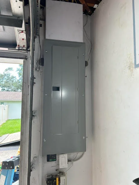 Gray electrical panel mounted on white wall with organized wiring and conduit connections