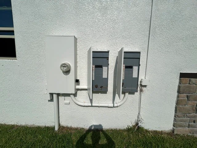 Electrical service panel and sub-panels with white PVC conduit on stucco exterior wall