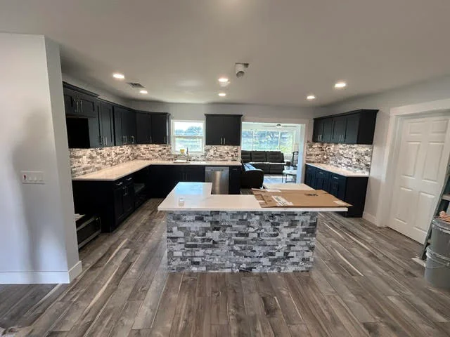 Kitchen with black cabinetry, stone backsplash, wood-look flooring, and recessed ceiling lights