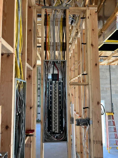 Electrical panel with organized breakers and yellow/black Romex cables routed through wooden framing