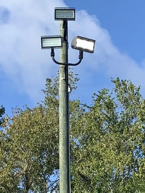 Three-head LED flood light fixture mounted on wooden pole with adjustable heads