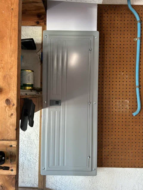 Gray metal electrical panel with vertical ribbed door installed in utility space with wood framing