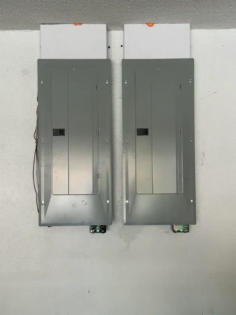 Two gray electrical panels with breaker switches mounted on white drywall