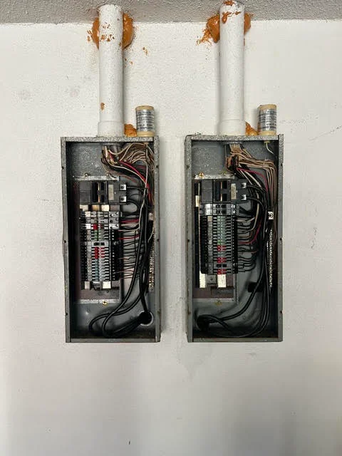 Two electrical panels with breakers, organized wiring, and white PVC conduit runs on drywall