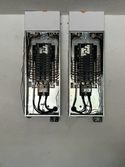 Two electrical panels with breakers and internal wiring installed on drywall